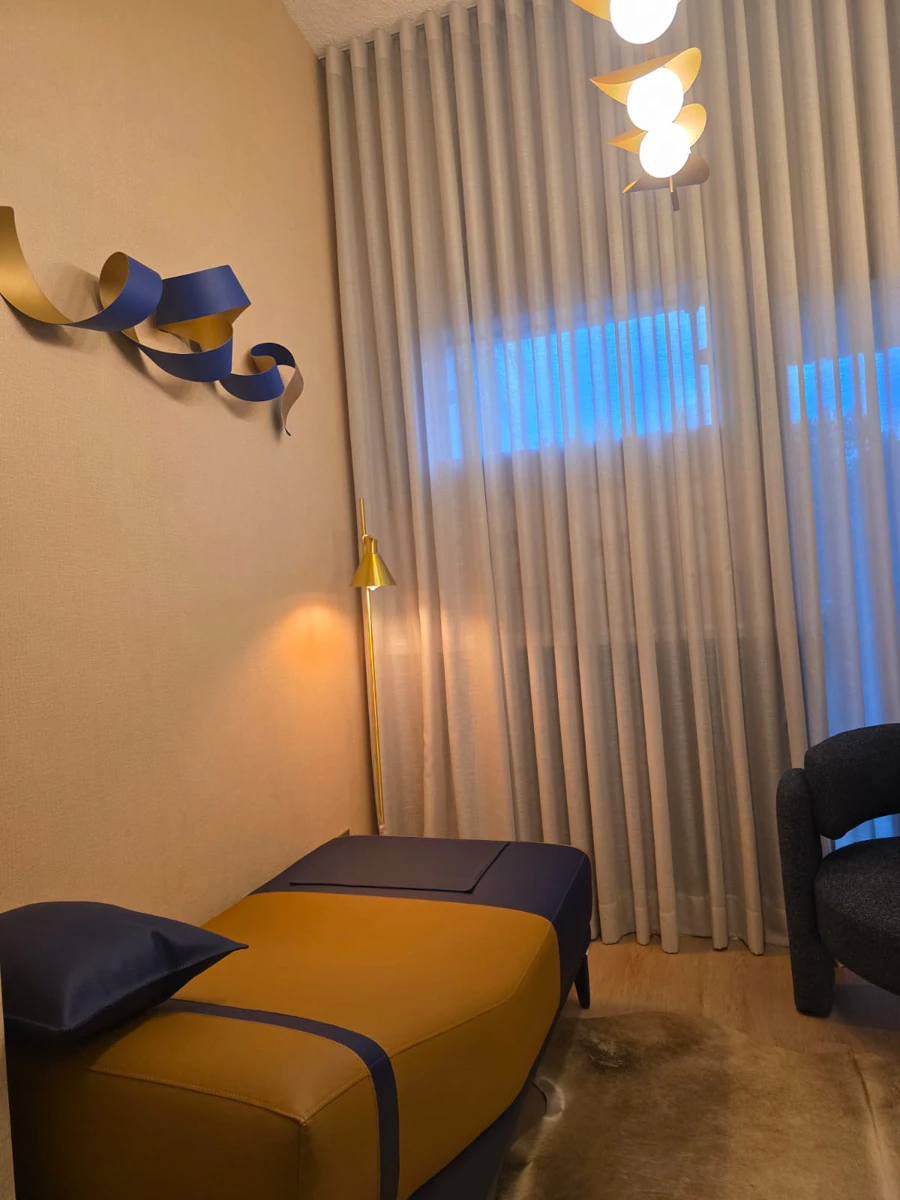 Divã em mostarda e azul-marinho ao lado da cortina, com luminária de piso dourada