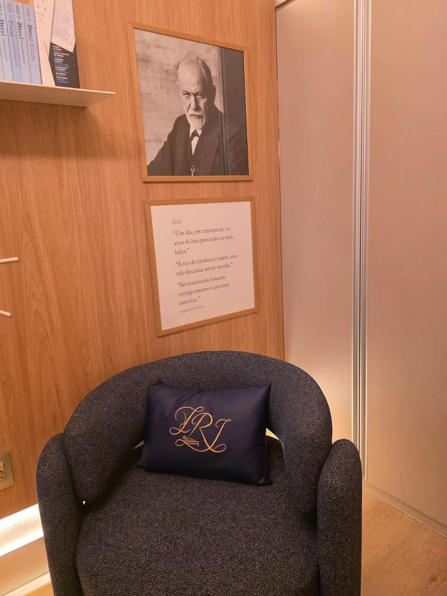 Poltrona com a almofada bordada com as iniciais da psicóloga, sob o retrato de Freud